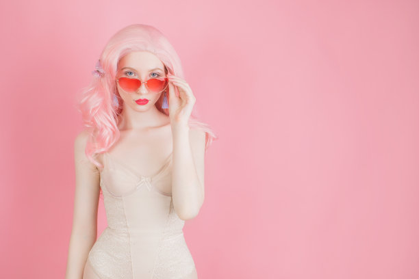 粉色头发的女人在假发在柔和的背景。美丽性感的女孩在夏天太阳镜和波浪假发。最小的趋势。柔和的颜色设计。戴着时髦太阳镜的女士。时尚风格。本空间图片下载