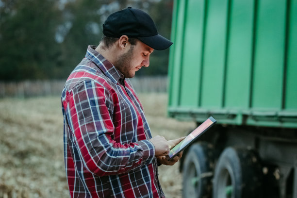 晚上，农民在平板电脑上查看联合收割机的收获进度图片下载