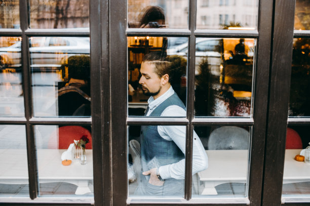 一名穿着灰色马甲的大胡子男子坐在餐厅窗外的肖像。图片下载