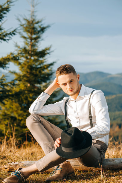 奢华的乡村风格的新郎坐在山的背景，把她的手靠近她的脸。图片下载