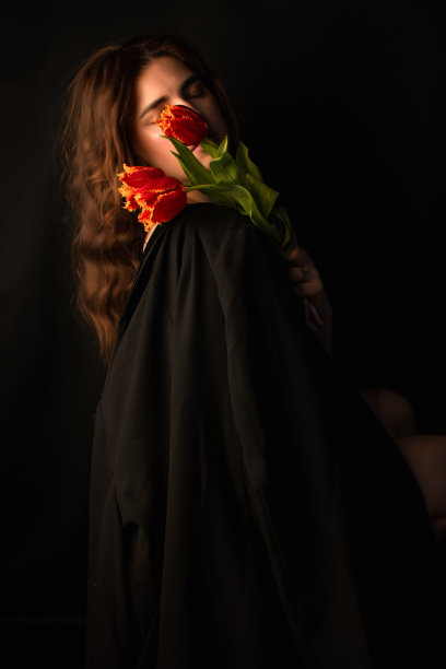 一名戴着墨镜的年轻女子的工作室肖像，背景是黑色的，手里拿着一束红色的郁金香。国际妇女节。情人节图片下载