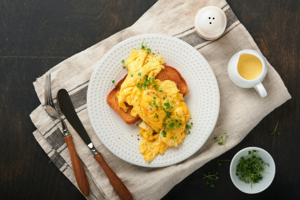 炒鸡蛋。松软黄油炒蛋面包配微绿萝卜和荷兰酱，白色盘子，深色的旧木头背景。自制早餐或早午餐。前视图。图片下载