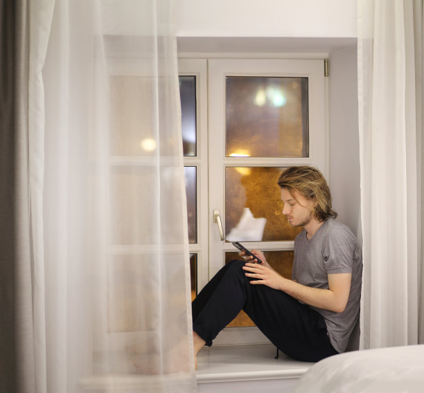 年轻人坐在窗台上玩智能手机图片下载