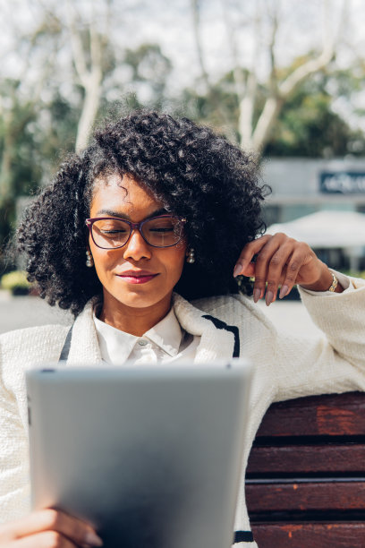 放松的女商人坐在公园的长椅上使用她的数字平板电脑图片下载