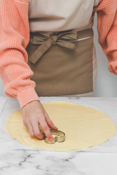 一个十几岁的白人女孩正在切一个金属心形的酥饼面团。图片下载