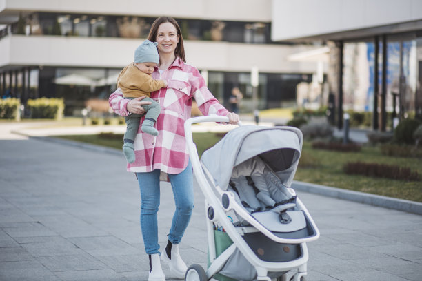 年轻的妈妈抱着婴儿，推着现代的婴儿车，漫步在城市中图片下载