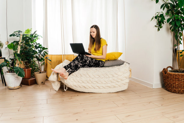 微笑的女人在家里的卧室里用笔记本电脑。图片下载