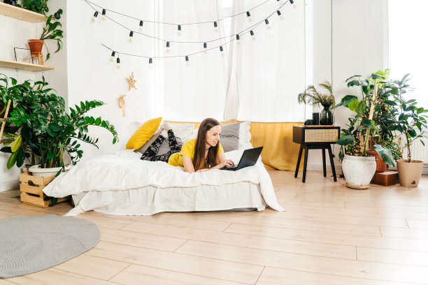 微笑的女人在家里的卧室里用笔记本电脑。图片下载