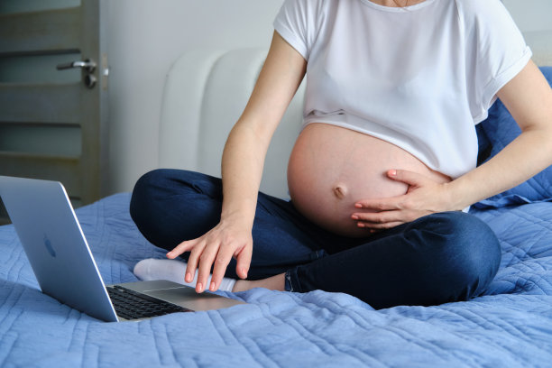 孕妇在家里的沙发上休息和使用在线技术的笔记本电脑工作。近距离图片下载
