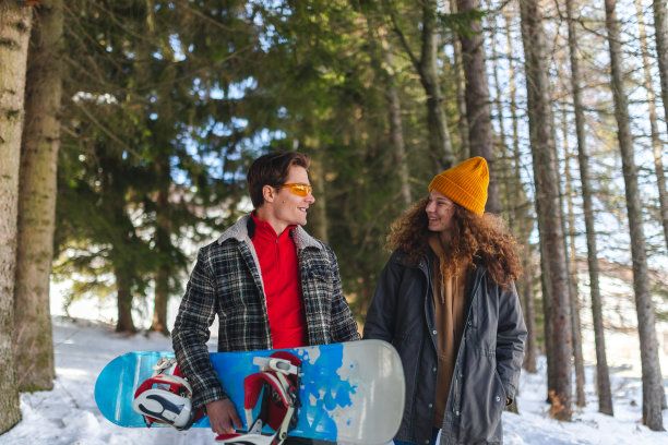 一对美丽的年轻异性恋情侣在雪原森林的小路上散步，手里拿着一块滑雪板图片下载