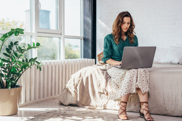年轻女子坐在床上，在卧室里使用笔记本电脑图片下载