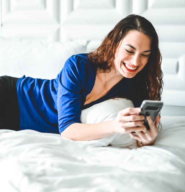 漂亮的年轻女人用手机放松在床上微笑和幸福的现代家庭图片下载