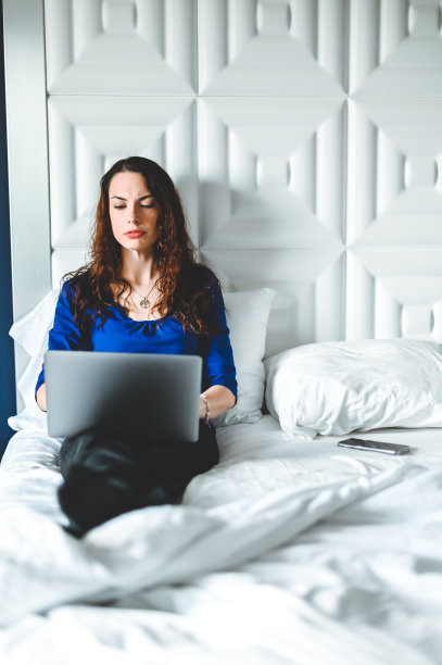 漂亮的年轻女子在床上使用笔记本电脑，在现代家庭中专注和认真图片下载