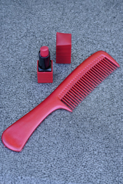 特写栗色的口红管帽和栗色的梳子超过焦点灰色的背景。图片下载