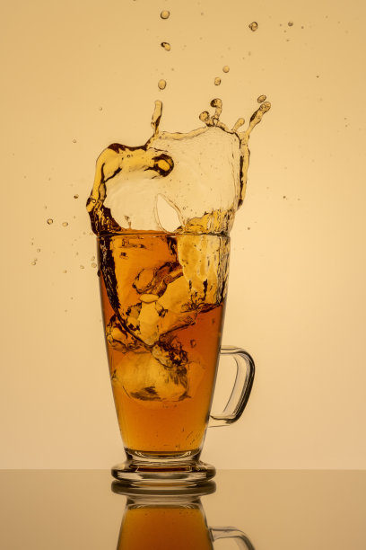 一杯冰茶和溅在黄色背景反射图片下载