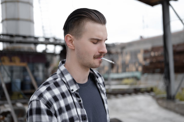 年轻英俊的男子，留着小胡子，穿着黑白格子衬衫，在外面抽烟。坏习惯图片下载