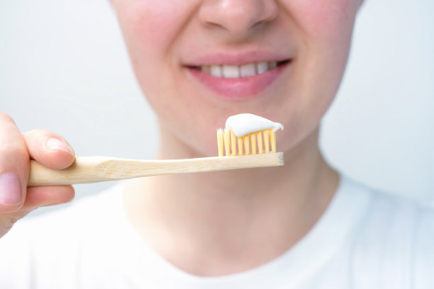 女孩拿着竹牙刷，牙膏在白色的背景上，选择性的聚焦。图片下载