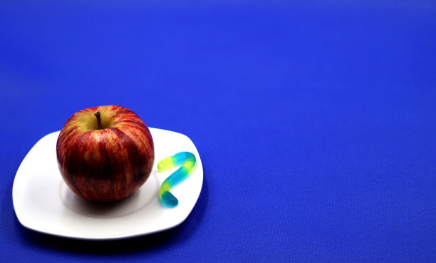 白色盘子与苹果和软糖蠕虫在蓝色背景为复制空间图片下载