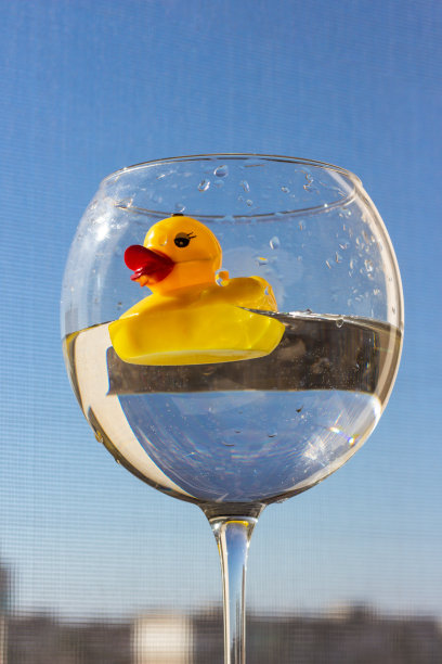 橡胶黄色的鸭子，大红色的嘴唇游泳在一个大的水对着蓝色的天空。度假和旅行图片下载