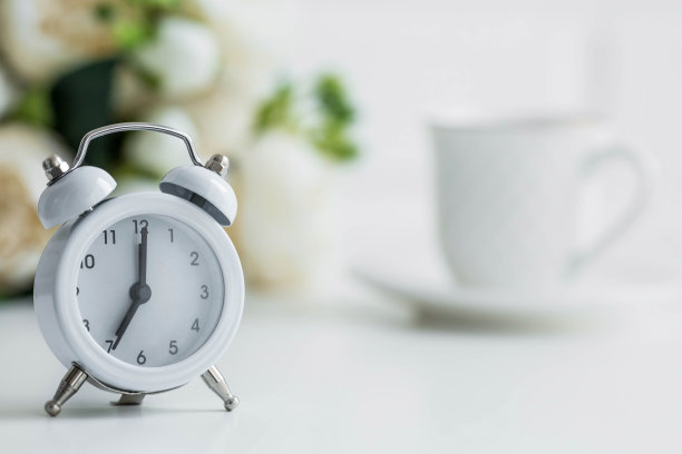 白色复古闹钟，白色砖墙背景上的鲜花和一杯咖啡。早上好时间的概念。图片下载