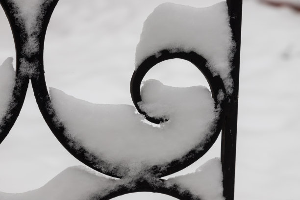 残缺不全的金属黑色栅栏被雪覆盖着图片下载