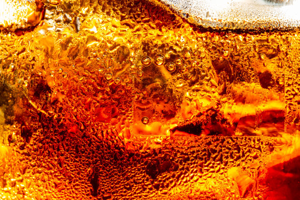 宏观的软饮质地，近距离观看在黑暗的可乐背景的冰块。清凉甜美的夏日饮品，泡沫和宏观气泡贴在玻璃墙上。图片下载