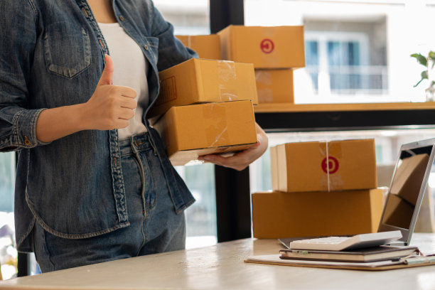 亚洲人用笔记本电脑在网上核对数字，销售初创企业、小企业主、电子商务概念，年轻女性则把物品打包运送给客户。图片下载