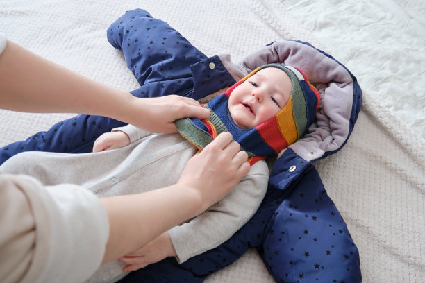 一位母亲为一个男婴戴上了一顶暖和的帽子。妈妈在床上给一个快乐的孩子穿上冬装。图片下载