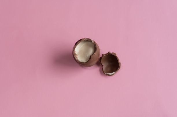 巧克力复活节蛋打破在柔和的粉红色背景与创意复制空间的一半。图片下载