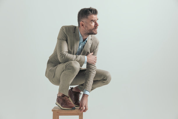 性感的大胡子男人肘撑膝蹲在木椅上图片下载