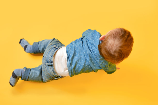 一个快乐的孩子在画室的黄色背景上穿着蓝色的衬衫和裤子。微笑的婴儿，穿着牛仔裤的小男孩图片下载