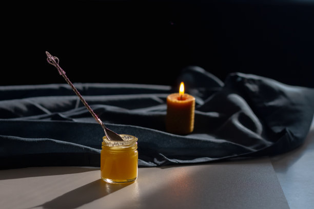 天然的蜂黄蜂蜜，装在玻璃罐中，用蜂房形状的蜡蜡烛和一勺蜂蜜放在蓝色的布上图片下载