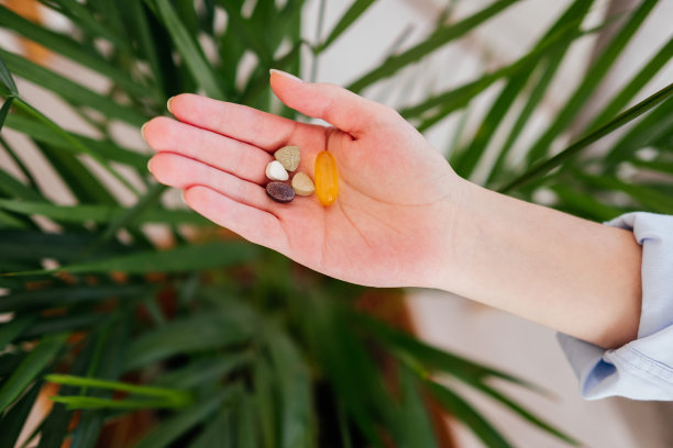 女性手握药丸，维生素欧米茄胶囊前的叶子俯视图室内。服药的概念图片下载