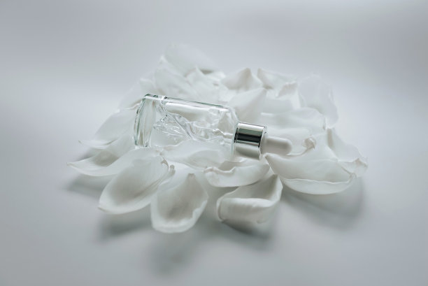白色的花瓣上放着一个透明的瓶子，里面装着面部精华液。图片下载