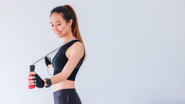 亚洲美丽微笑的妇女运动与跳绳白色墙壁健身背景。运动减肥，增加弹性，收紧体形。健康的生活方式的概念。图片下载