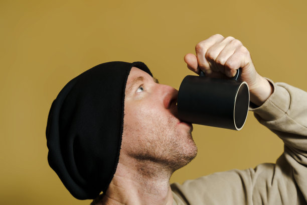 白人从一个黑色的杯子里喝水，一个戴着黑色帽子的年轻人的肖像，特写镜头图片下载