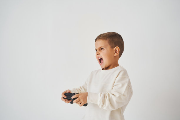感情用事的孩子，游戏手柄在白色背景上。男孩在玩游戏。图片下载