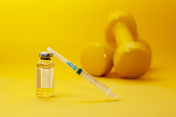 黄色背景下，一个注射器和一罐液体放在一个哑铃旁边，这是一张水平的图片。在体育运动中使用兴奋剂的概念，类固醇、睾酮和其他在体育运动中禁用的药物。图片下载