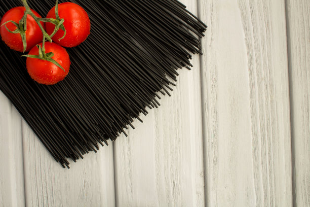 黑色意大利面和樱桃在灰色的木制背景。俯视图。复制空间。图片下载