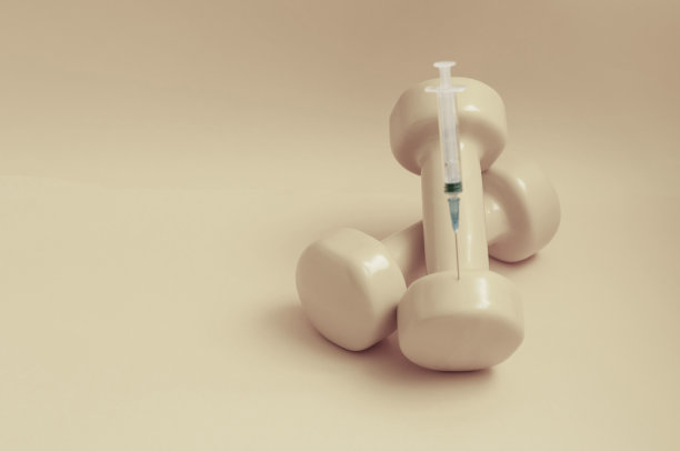 注射器卡在一个哑铃上黄色背景，水平拍摄，复制空间。在体育运动中使用兴奋剂的概念，类固醇、睾酮和其他在体育运动中禁止使用的药物。图片下载
