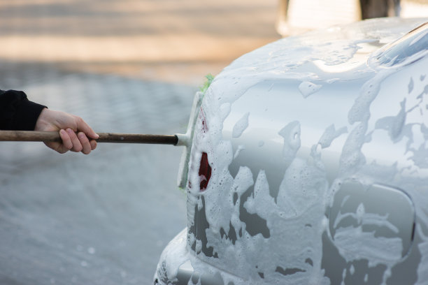 一名男子在自助洗车店用刷子清洗起泡的汽车，特写镜头图片下载