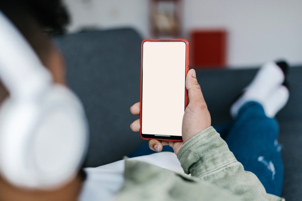 一个年轻人躺在沙发上，手里拿着的手机屏幕是空白的图片下载