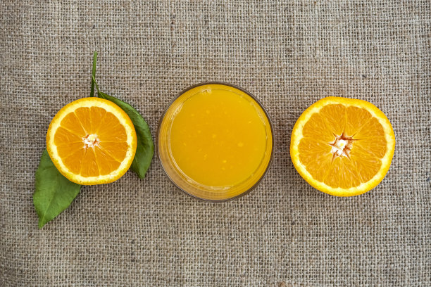 切一半的橙子和一杯果汁在麻袋织物上图片下载