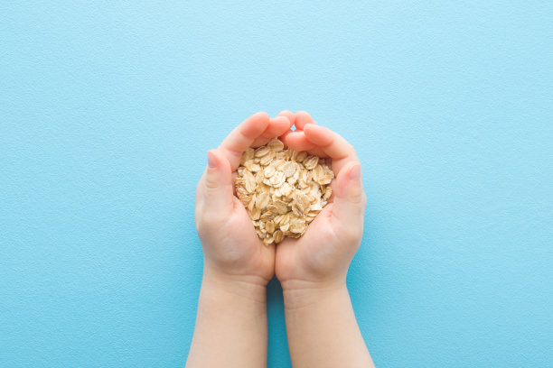 婴儿的手握干燕麦卷在浅蓝色的桌子背景。柔和的颜色。特写镜头。视角拍摄。儿童健康食品。自顶向下的观点。图片下载