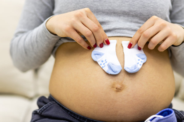 裁剪照片孕妇赤裸的胃与小的孩子袜子。图片下载