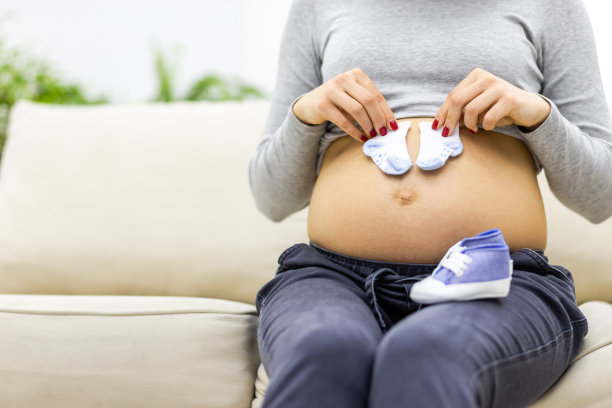 裁剪照片孕妇赤裸的胃与小的孩子袜子。图片下载