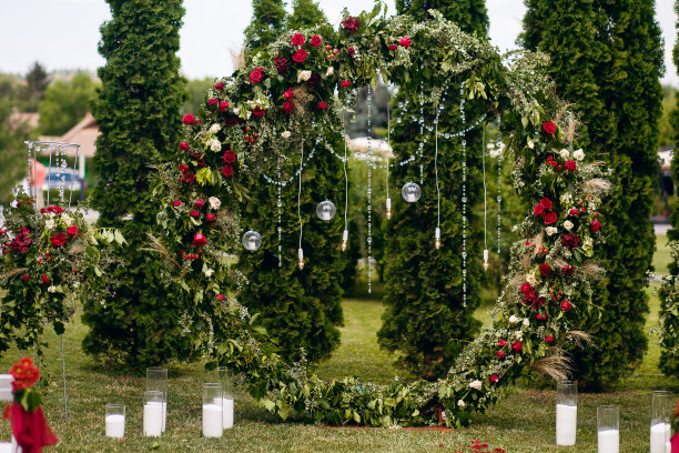 一个绿色的圆形婚礼拱门被鲜花装饰着，鲜花矗立在绿色的草坪上的森林里图片下载