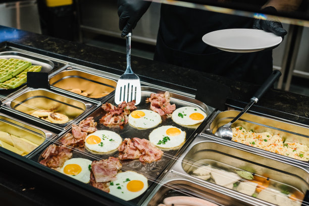 男服务员或女服务员把食物放在盘子里。自助早餐，家庭早午餐。人们在豪华餐厅的室内提供自助餐。餐饮和餐饮。庆祝晚会。图片下载