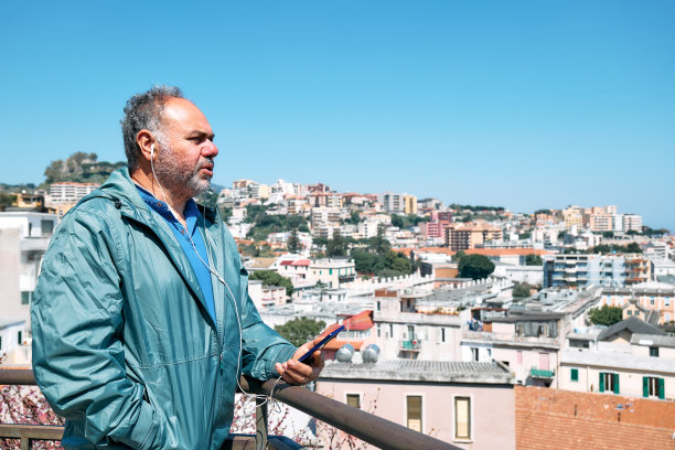 英俊成熟的大胡子男人一边说着手机，一边欣赏着意大利西西里岛墨西拿的全景。城市旅游休闲。图片下载