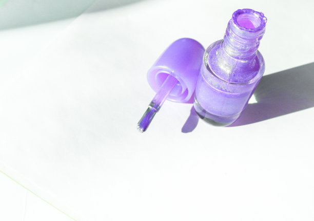 一个开着的瓶子上涂着淡紫色的指甲油，旁边还有一把刷子，在白色的表面上投下阴影，时尚美的概念图片下载